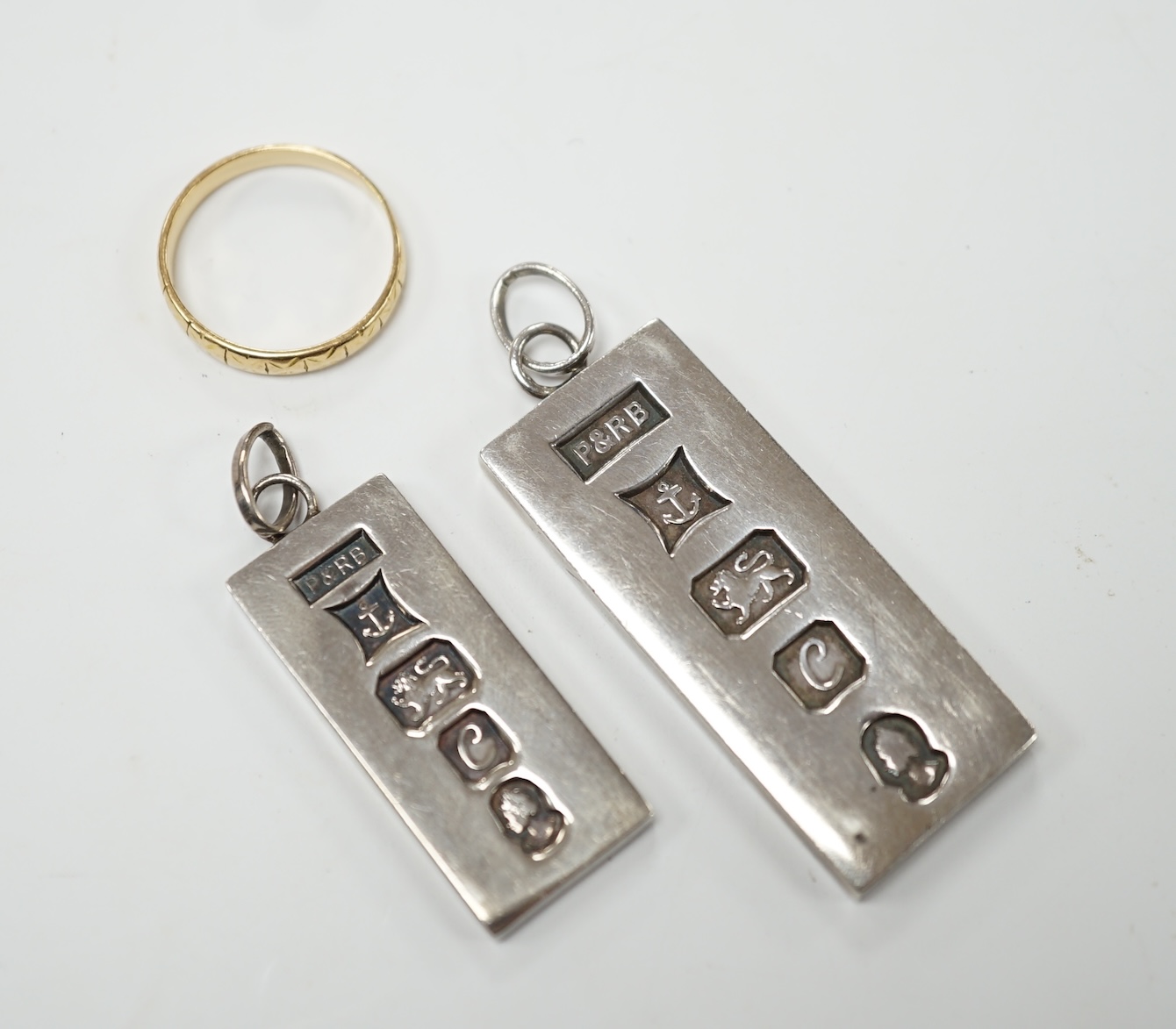 A 1920's engraved 18ct gold wedding band, 2.5 grams, together with two silver ingot pendants. Fair condition.